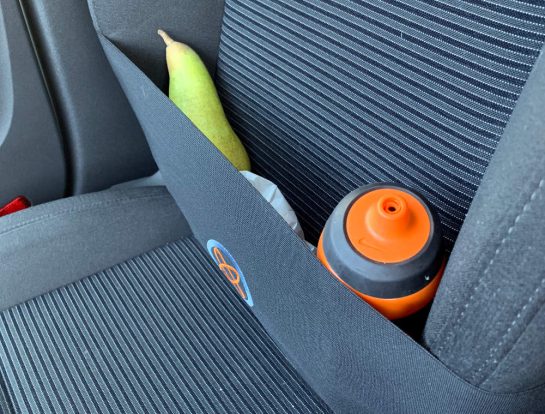 Beifahrersitz mit Gummidings um. Darin stecken eine Birne, eine Brottüte und eine Trinkflasche.