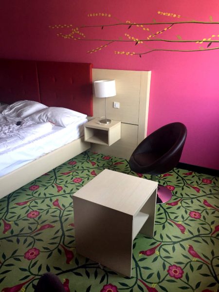 Hotelzimmer: Pink gestrichene Wand mit Blumenranken, hellgrüner Teppich mit Blumen und Vögeln in Pink