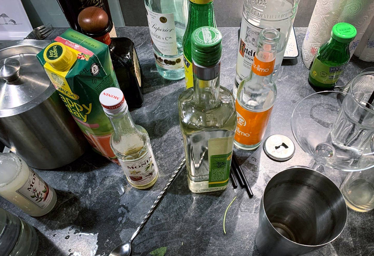 Flaschen und Safttüten auf der Küchenanrichte, ein Cocktailshaker, ein Löffel, diverse Utensilien