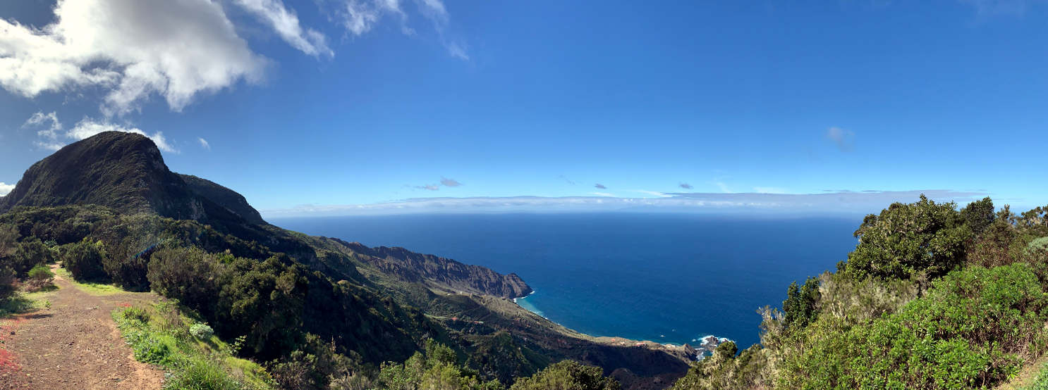 Panoramabild: links Lehmpfad und ein Hügel, in der Mitte das Meer. 