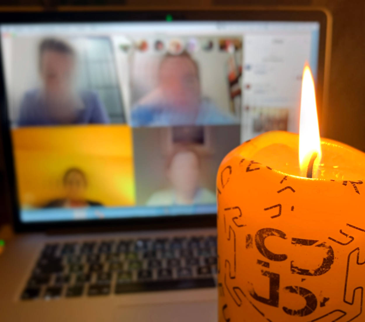 Im Vordergrund eine brennende Kerze, im Hintergrund eine Webkonferenz, unscharf