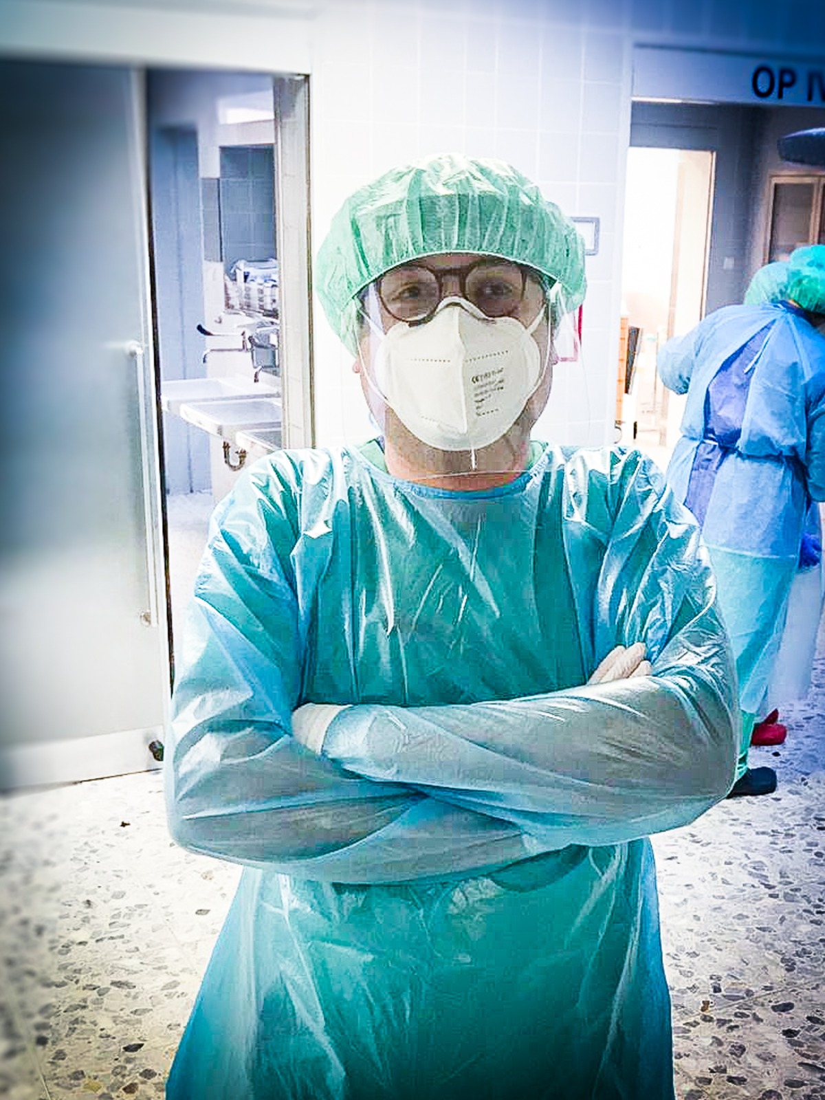 Mann in mediziner Schutzkleidung mit Kittel, FFP2-Maske, Faceshild und Haube in einem Krankenhausflur