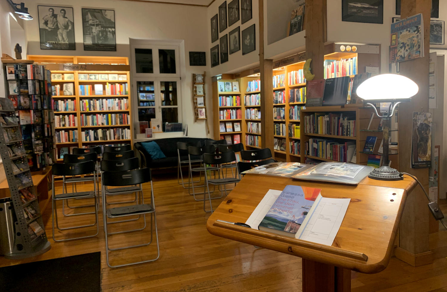 Holzpult mit leselampe in einer Buchhandlung. Im Hintergrund leere Stühle und Bücherwände. 