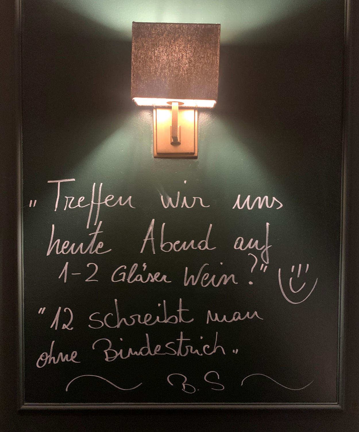 Tafel im Restaurant, Text: "Treffen wir uns heute abend auf 1 - 2 Gläser Wein?" - "12 schreibt man ohne BIndestrich."