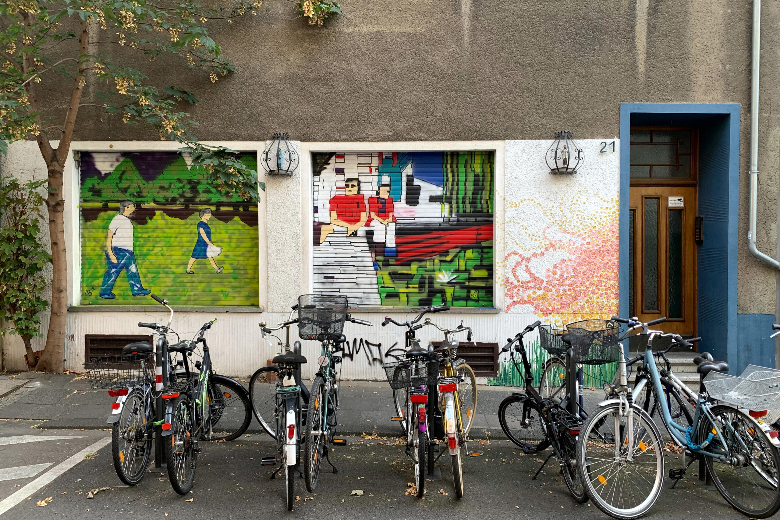 Fahrräder vor einer Fassade, die Rolläden der Fenster haben Graffiti-MOtive