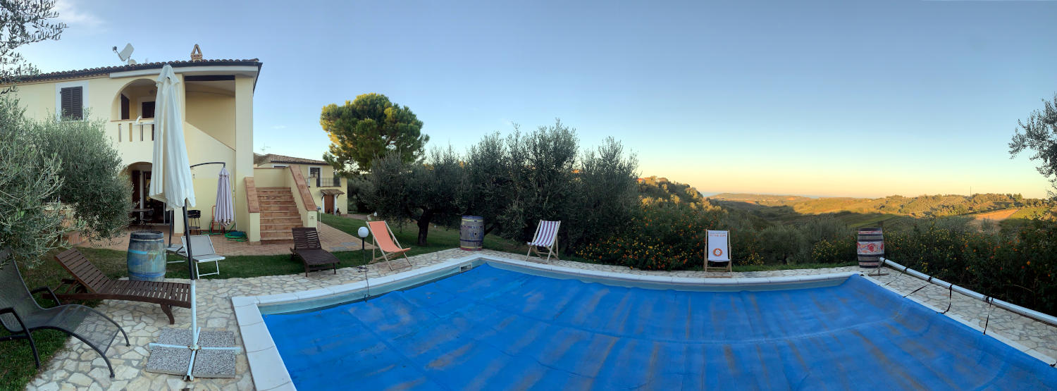 Panoramabild: Haus, abgedeckter Pool, in der Ferne die Abendsonne. 