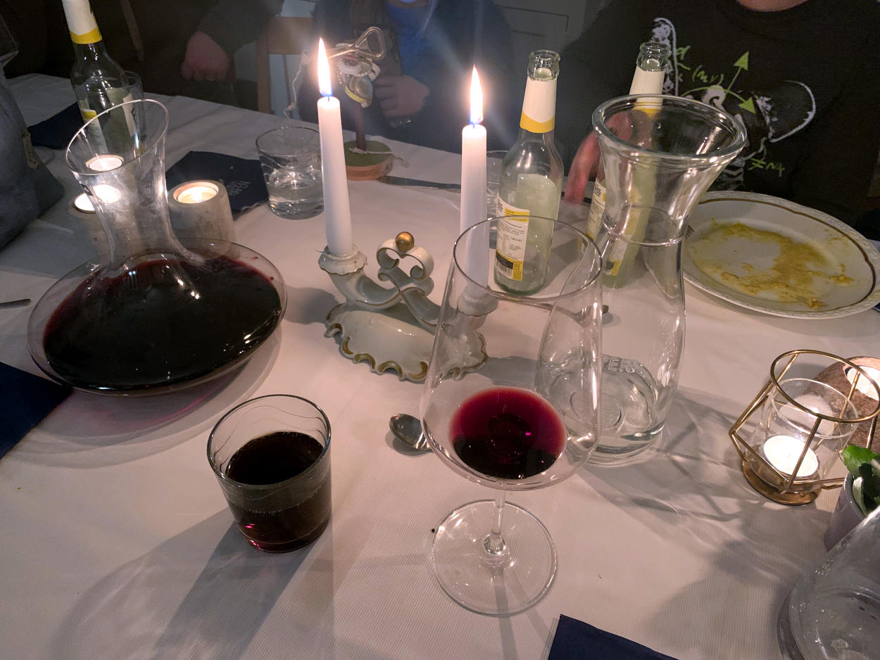 Ein Dekanter mit Rotwein, Kerzen, leeren Flaschen und einem Glas Cola auf einer weißen Tischdecke