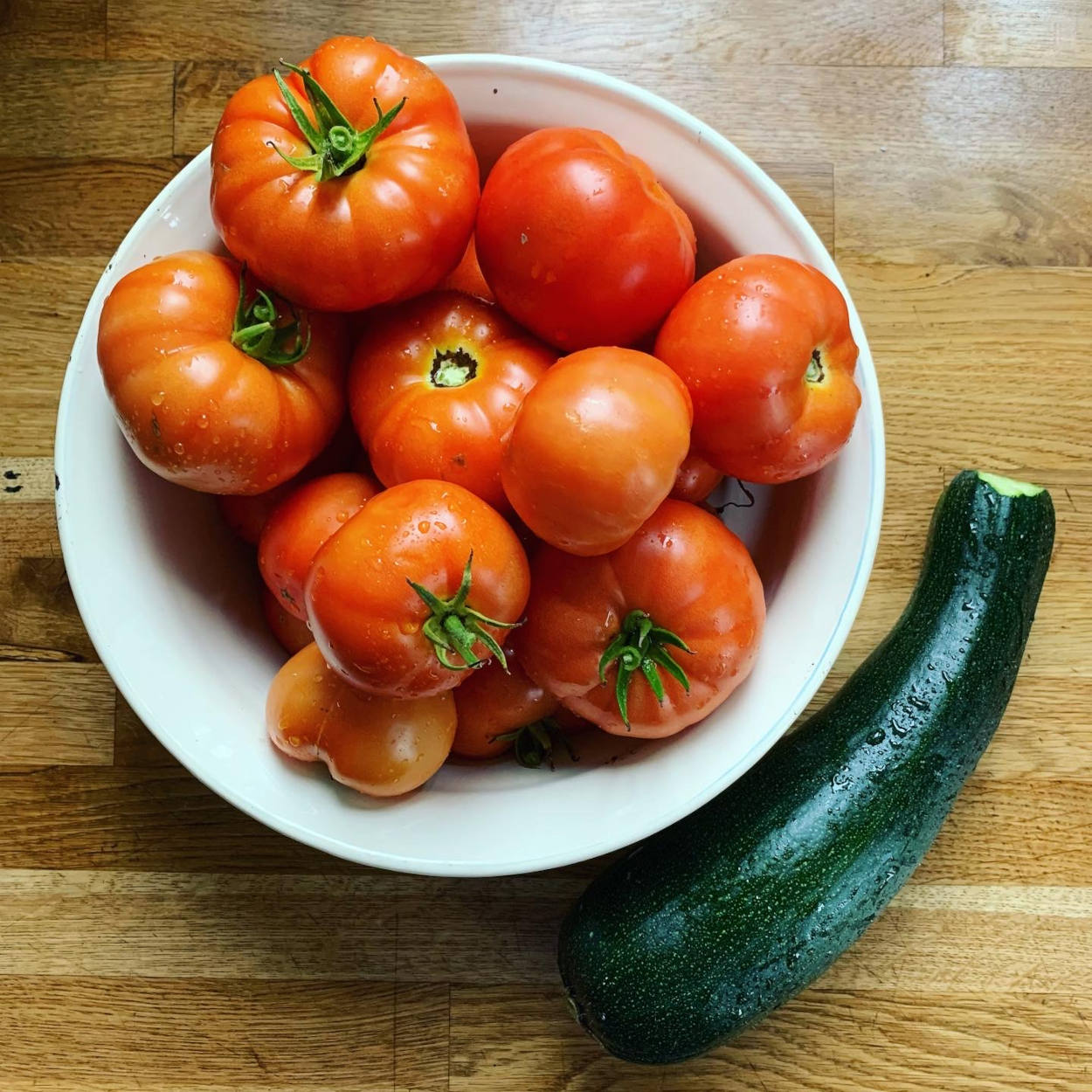 Tomaten in einer Schüssel, daneben eine Zucchini