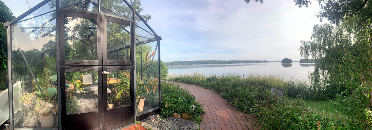 Panorama-Aufnahme eines Gewächshauses mit Sitzgelegenheit und See