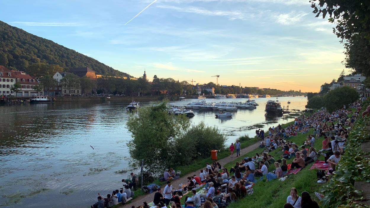 Abendstimmung am Neckar. Auf den Neckarwiesen sitzen viele Menschen.