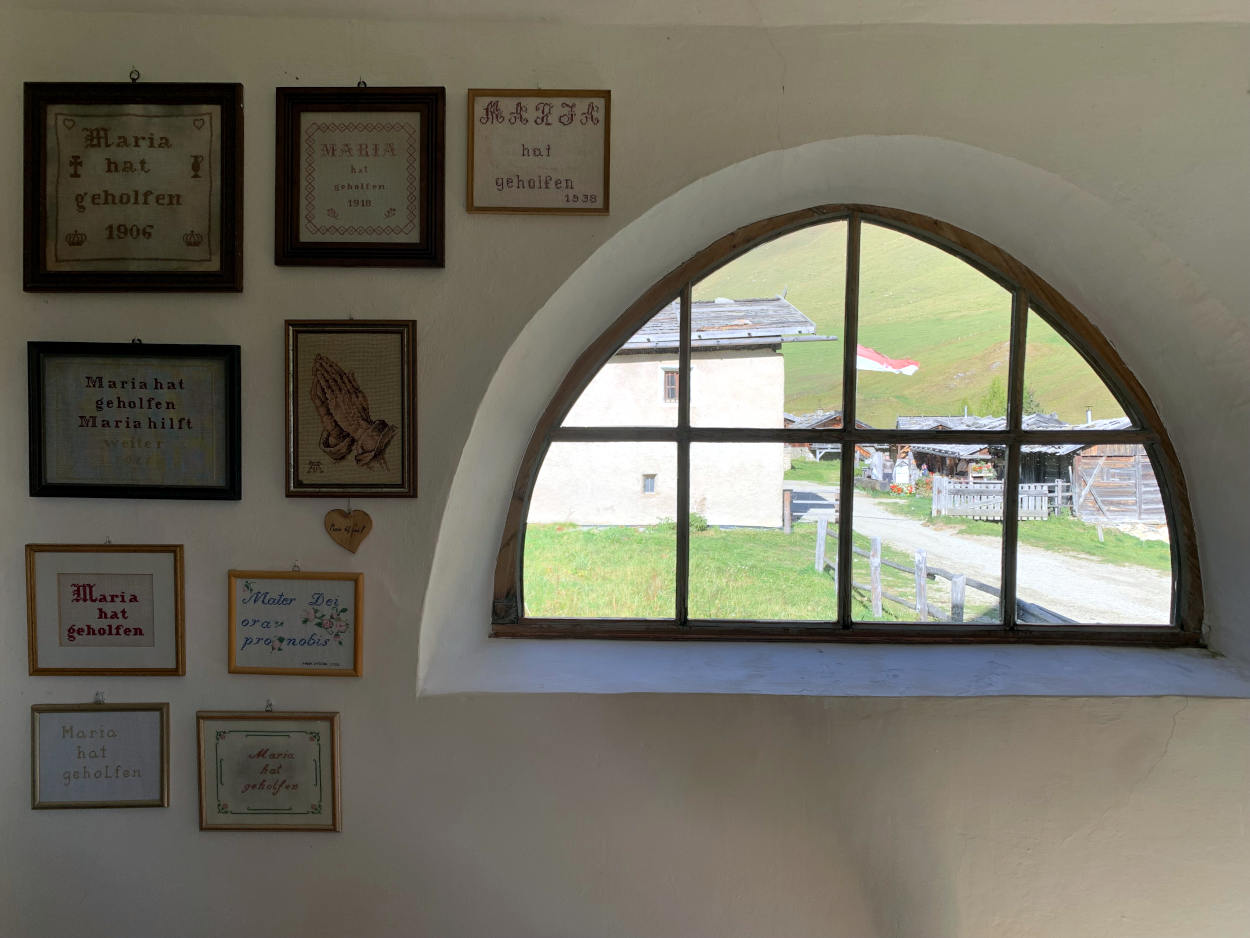 Fenster in einer Kapelle, daneben gestickte Bilder mit dem Text "Maria hat geholfen"