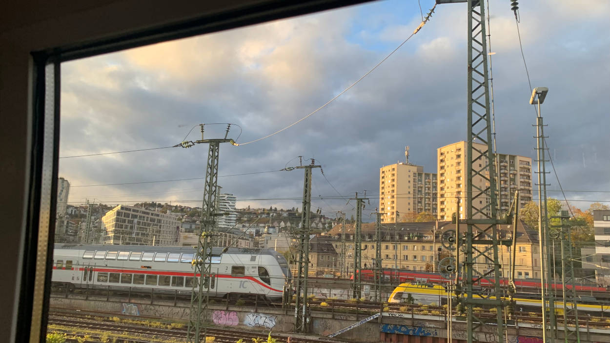Blick aus dem Zugfenster auf die Gleise vor Stuttgart. Im Vordergrund Züge, im Hintergrund ein wilder Himmel