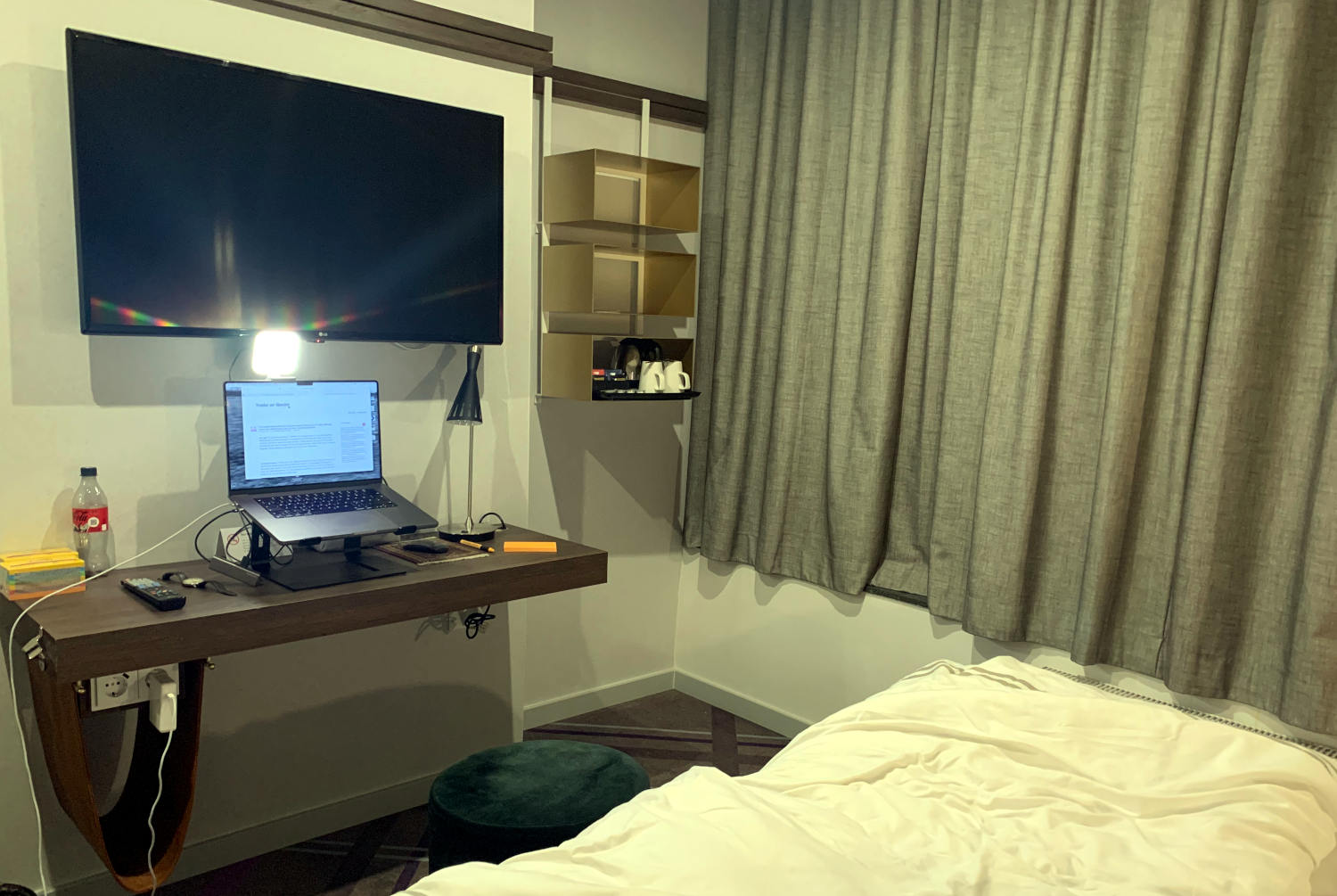 Schreibtisch im Hotel unter einem Fernseher, darauf ein Laptop auf einem Ständer und ein Licht für Videokonferenzen. 