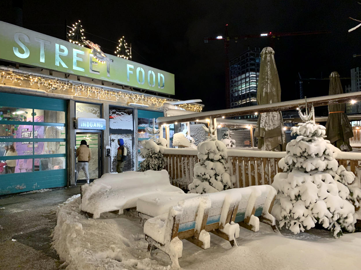 Street-Food-Halle von außen, davor schneebedeckte Bänke