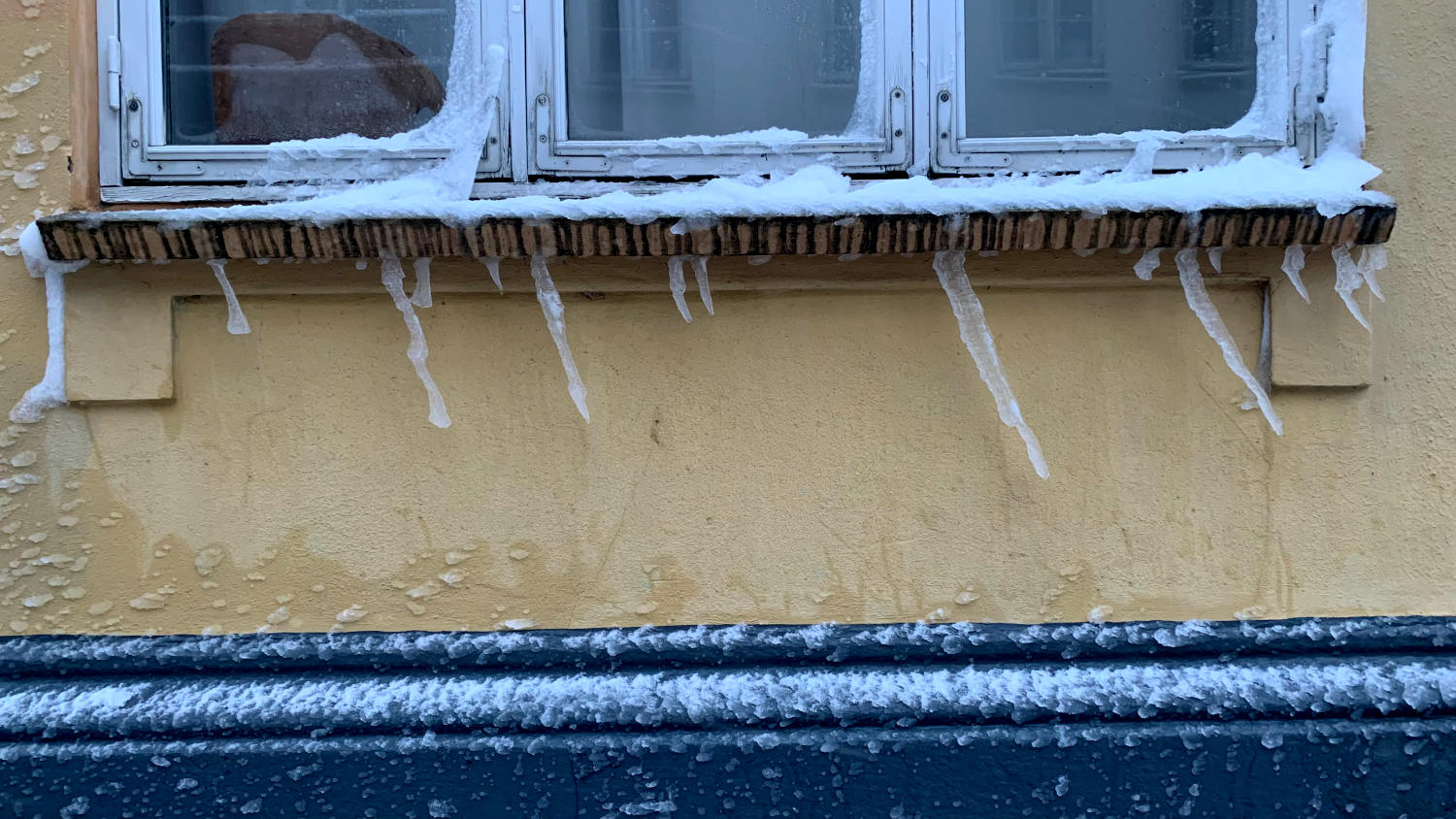 Eiszapfen wachsen schräg von einer Fensterbank 
